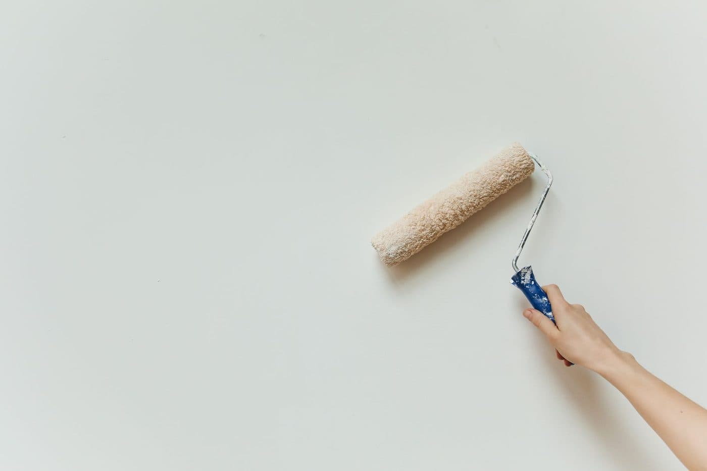 Peintre appliquant une deuxième couche de peinture blanche au rouleau sur un mur