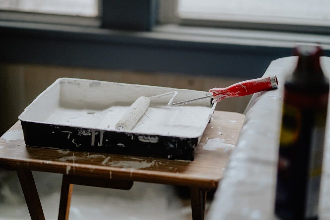 Pot de peinture écologique et pinceau posés sur une bâche de protection dans un appartement en travaux